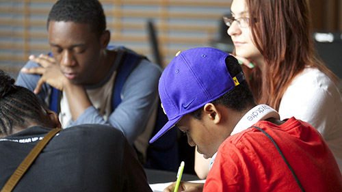 Students from Chicago Southside taking notes. They are of a variety of skin colors, hair color, and clothing color.